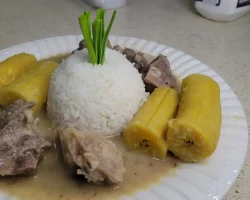 Traditional Filipino pork stew with rice and plantains on a white plate.